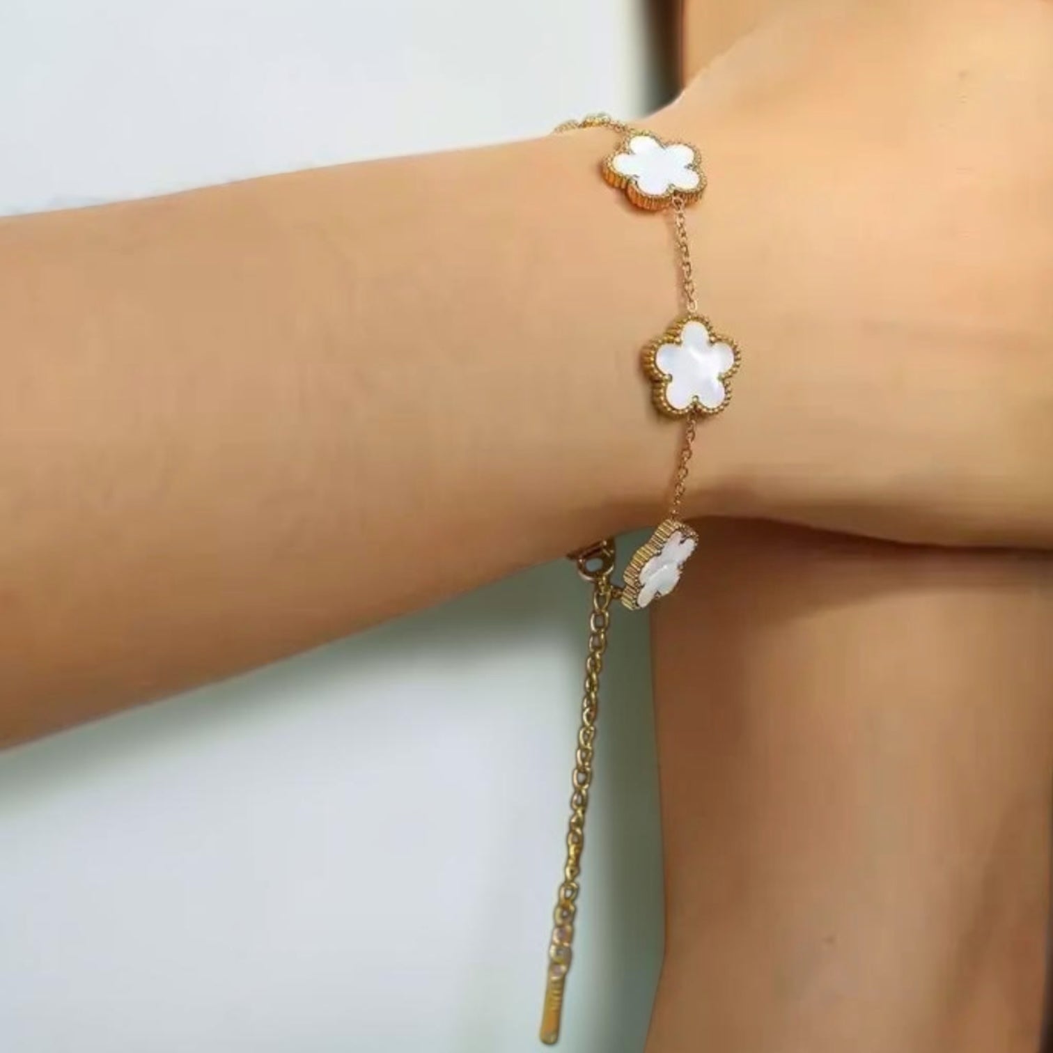 Gold bracelet with white flower charms on a wrist against a light background