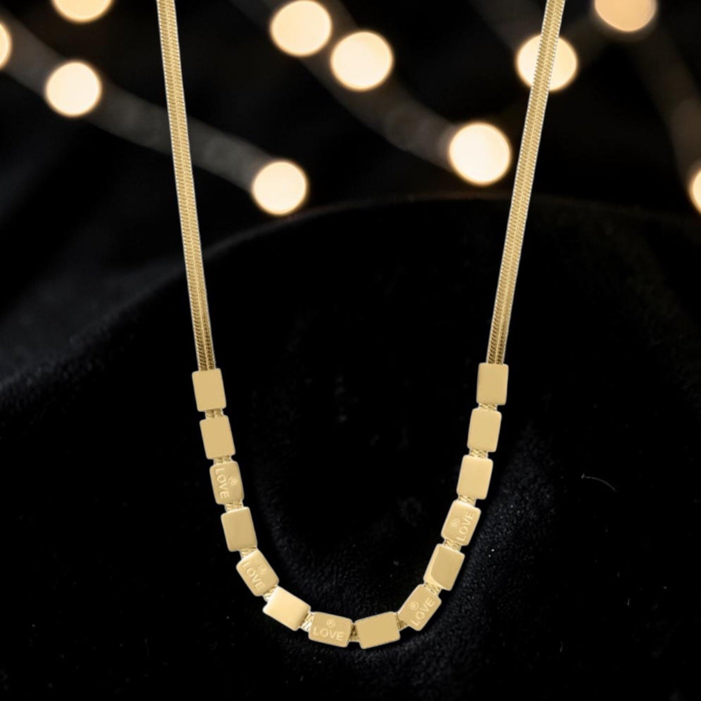 Gold necklace with square beads on a black background with blurred lights